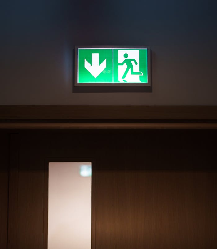 Green emergency exit sign with arrow above a closed door for evacuation purposes.